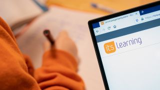 Die Website der Lernplattform "itslearning" ist auf einem Notebook zu sehen, während im Hintergrund ein Kind am Schreibtisch sitzt. (Quelle: dpa/Florian Schuh)