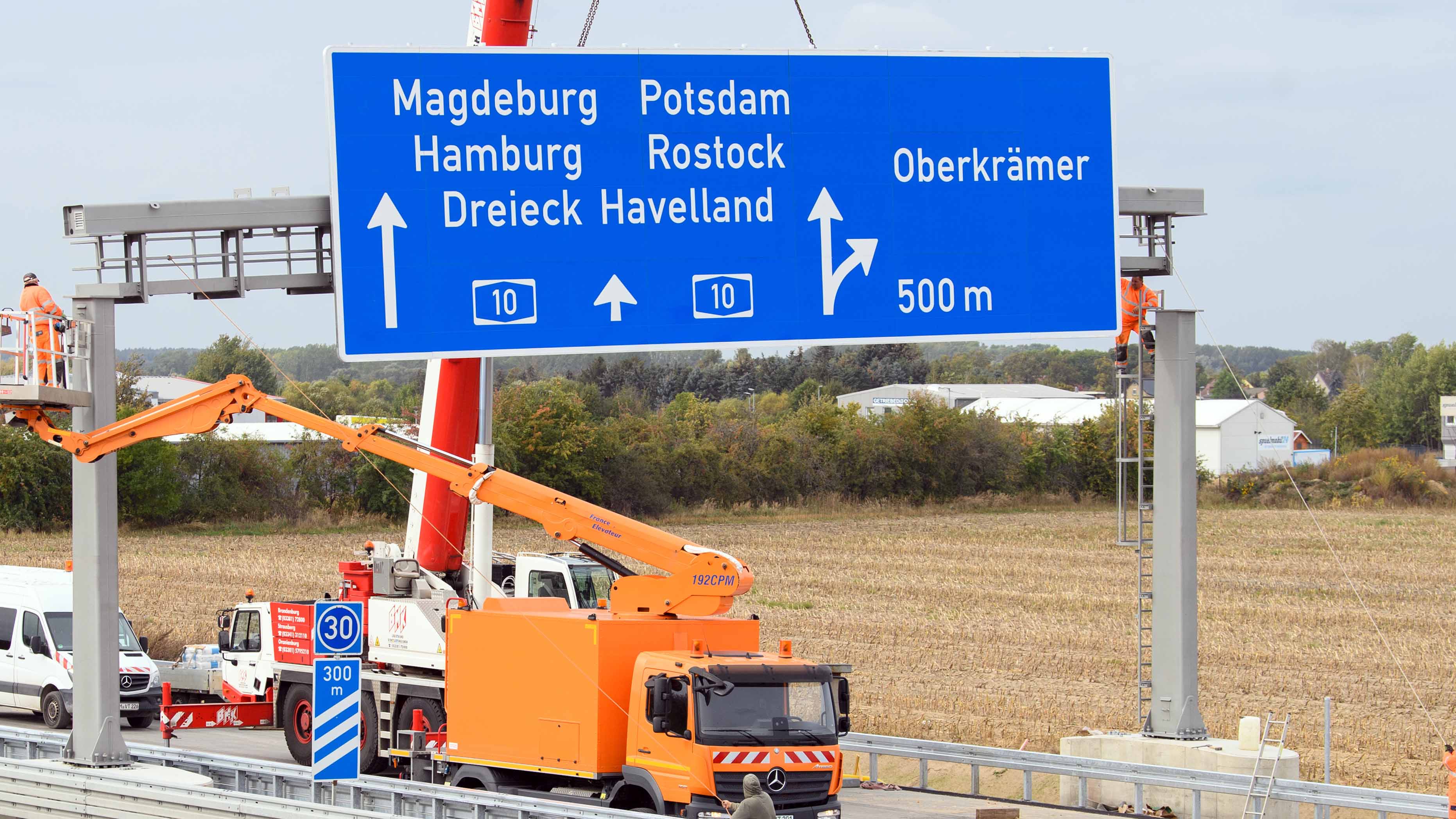 Arbeiter installieren auf der A10 etwa 300 Meter vor der Abfahrt nach Vehlefanz ein Schild mit dem Hinweis auf das Autobahndreieck Havelland und die Fahrtrichtungen Magdeburg, Hamburg, Potsdam und Rostock.