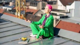 Symbolbild: Eine Frau meditiert auf dem Dach eines Wohnhauses. (Quelle: dpa/A. Antoniadis)