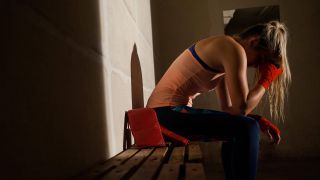 Junge Frau sitzt niedergeschlagen in Sportumkleide und stützt Kopf (Bild: Imago/Panthermedia)