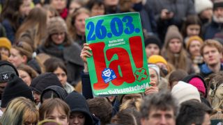Ein Teilnehmer der Demonstration von Fridays for Future hält einen Plakat mit der Aufschrift „26.03. Berlin 2030 klimaneutral. Ja zum Volksentscheid“ hoch. (Quelle: dpa/Monika Skolimowska)