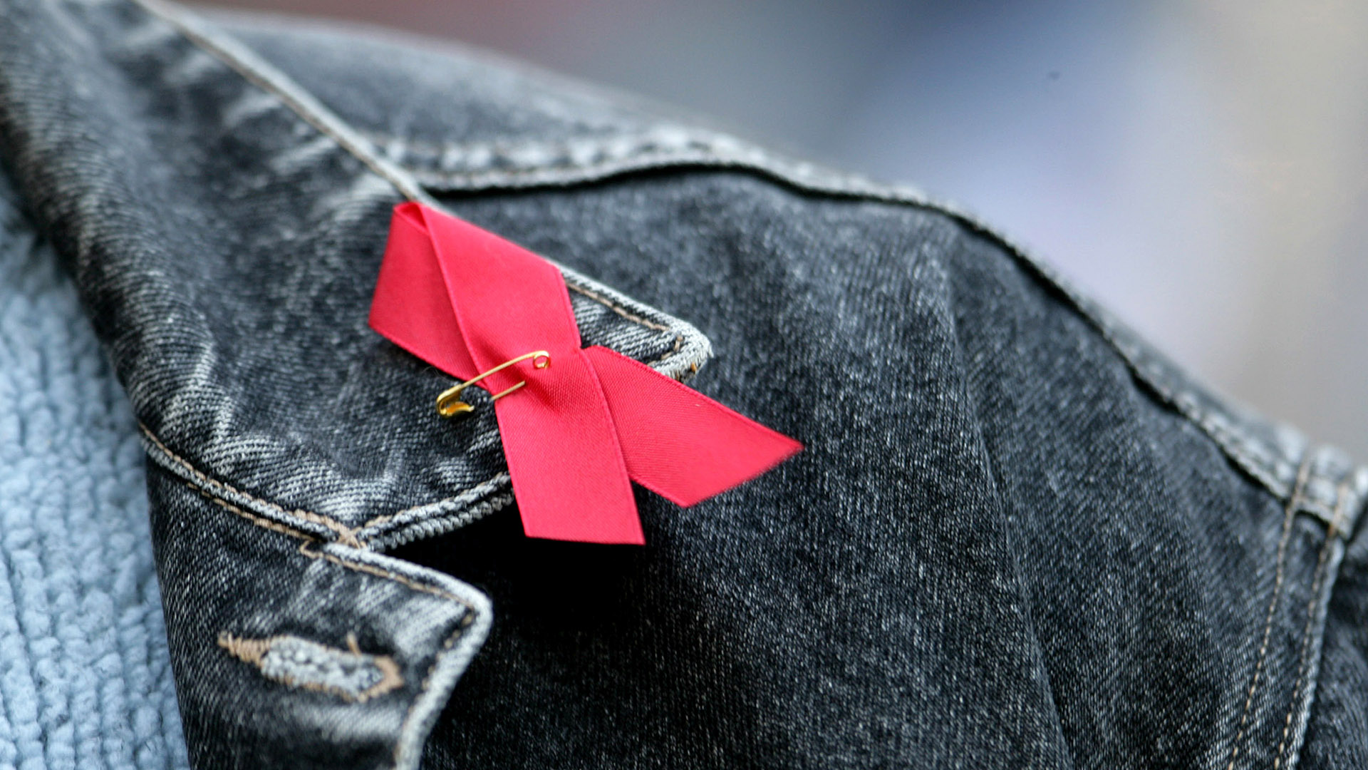 Symbolbild:Die Rote Aids-Schleife ist an eine Jacke geheftet. Die Rote Schleife ( englisch Red Ribbon ) ist weltweit ein Symbol der Solidarität mit HIV-Infizierten und AIDS-Kranken.(Quelle:picture alliance/R.Goldmann)