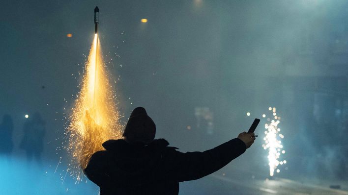Symbolbild: Während er mit der linken Hand eine brennende Rakete hält, filmt sich ein Mann bei der Aktion selbst mit seinem Smartphone. (Quelle: dpa/Roessler)