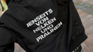 Symbolbild: Eine Aufschrift "Jenseits von Nelken und Pralinen" auf einer Jacke. (Quelle: IMAGO/Müller-Stauffenberg)