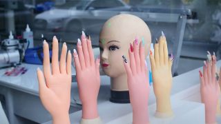 Symbolbild: Kunststoffhaende mit lackierten bunten Fingernaegeln als Muster und ein Puppenkopf stehen im Schaufenster eines Nagelstudios in Berlin. (Quelle: dpa/Steinberg)