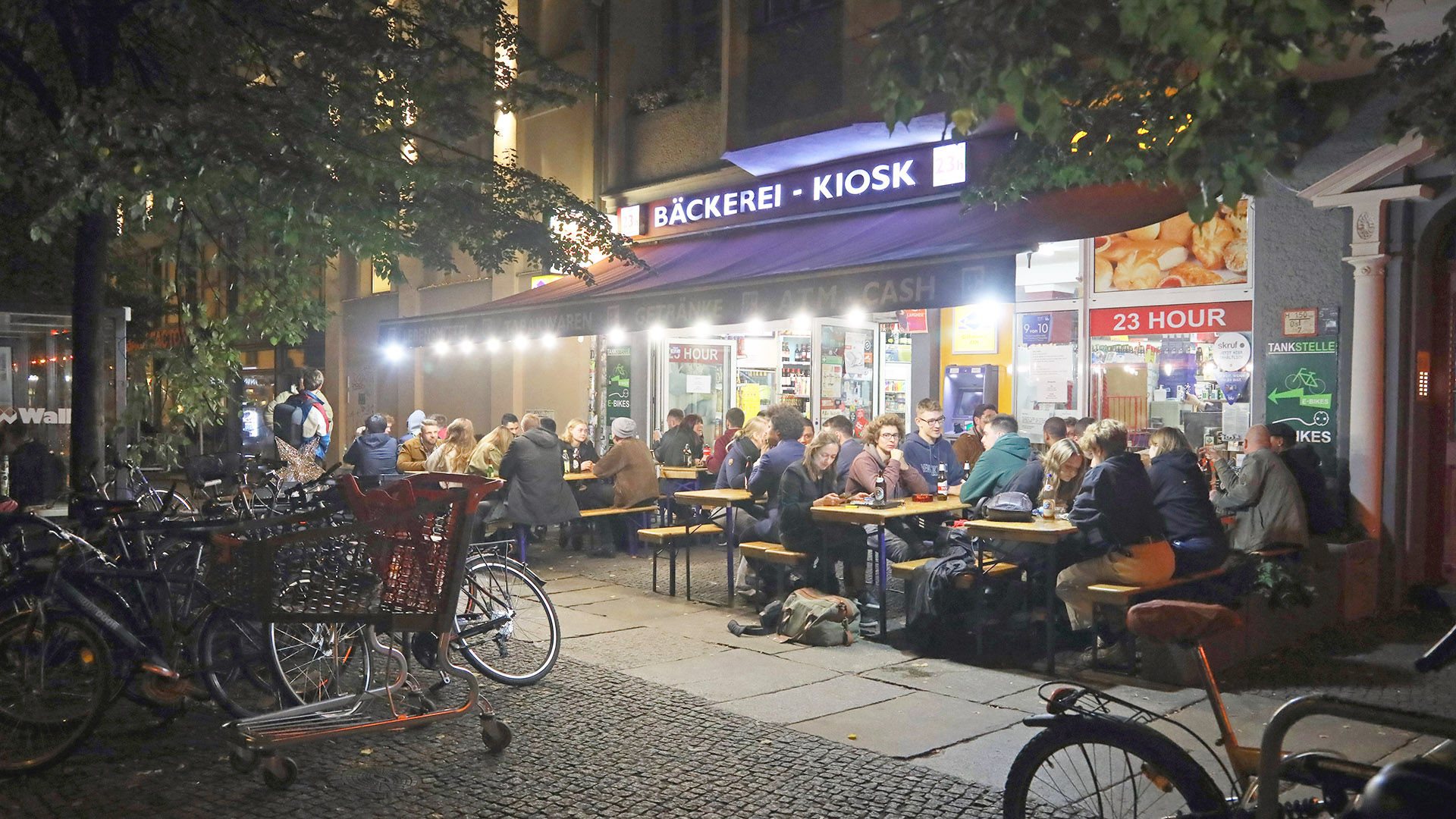Archivbild: Junge Leute sitzen nachts in Berlin vor einem Kiosk / Spätkauf. (Quelle: imago images/Gudath)