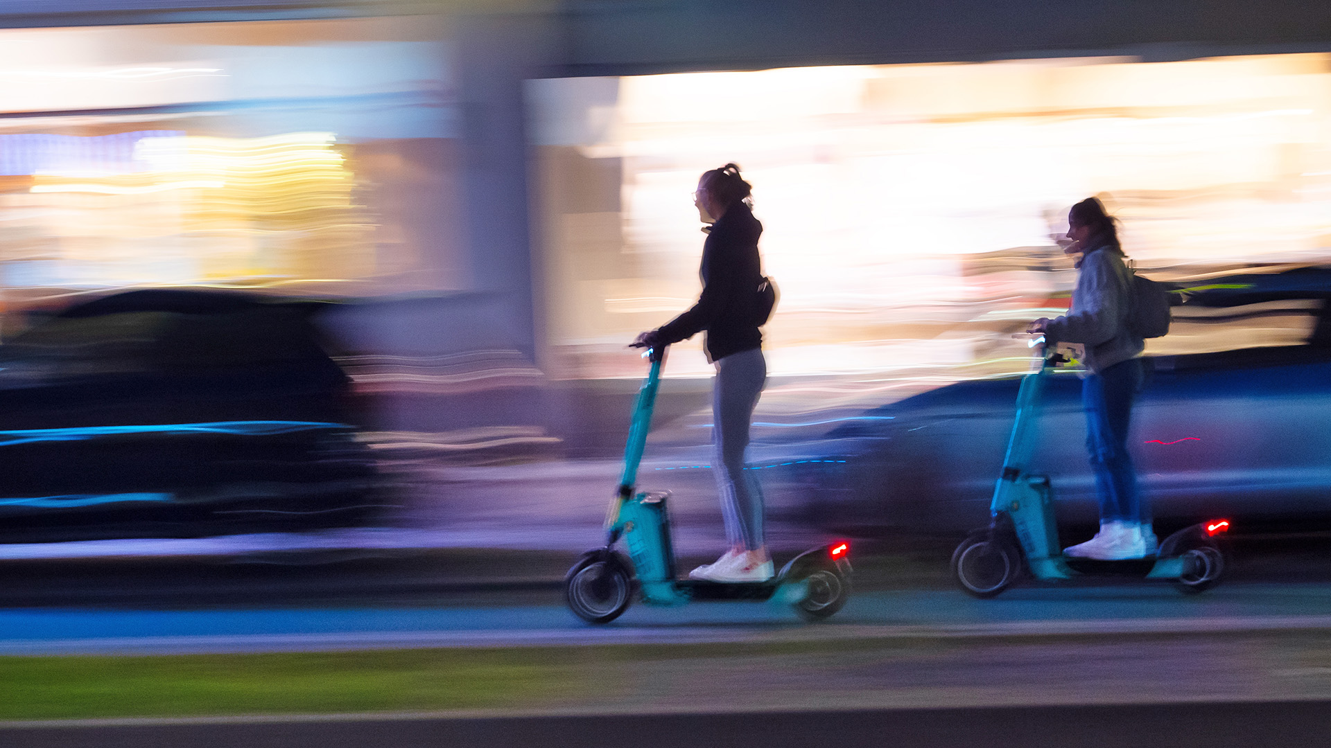 Symbolbild: Zwei Junge Frauen fahren am 23.09.2023 auf E-Scootern nach Einbruch der Dunkelheit auf einer Hauptstrasse in Berlin. (Quelle: dpa/Wolfram Steinberg)