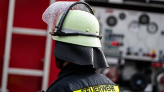 Symbolbild: Ein Feuerwehrmann steht mit Schutzkleidung und Helm vor einem Einsatzfahrzeug. (Quelle: imago-images/Silas Stein)
