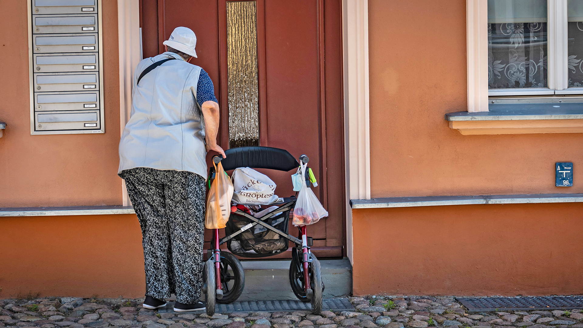 Eine alte Frau mit Rollator steht am 07.06.2022 vor einer Tür in Neuruppin in Brandenburg. (Quelle: Imago Images/Jürgen Ritter)