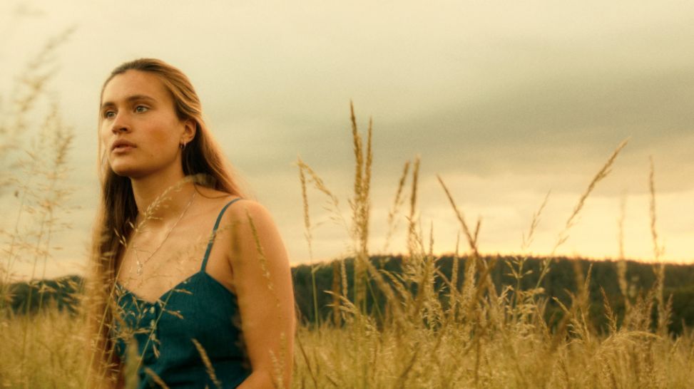 Junge Frau links im Bild, steht in einem Getreidefeld. Szene aus dem Kinofilm "Irgendwann werden wir uns alles erzählen" (Bild: rbb/Pandora Film/Row Pictures)
